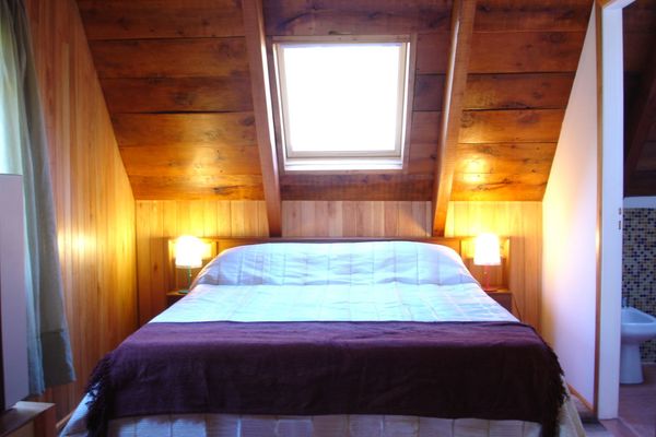 Interior de la habitación Coihue en la hostería Wesley, con cama doble, techo de madera y una ventana cenital que permite la entrada de luz natural