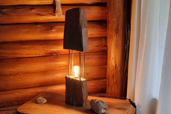 Interior cálido y acogedor de una cabaña rústica ubicada en Potrerillos, Mendoza, Argentina, sobre el Río Mendoza, en el km 1108 de la Ruta Internacional N°7. La imagen muestra una atmósfera de montaña con paredes y techo de troncos, una lámpara artesanal