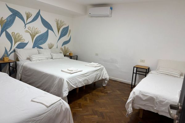 Dormitorio luminoso con varias camas, veladores con lámparas cálidas y detalles naturales. Vista desde una pequeña abertura decorada con plantas que aporta un toque acogedor y relajado. Ideal para descansar en un ambiente sereno. Baño privado en Suite.