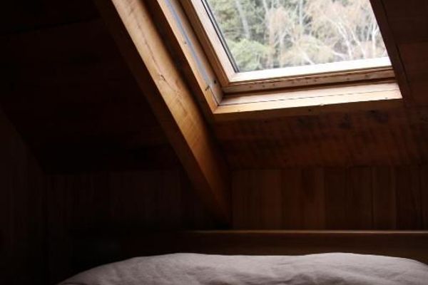 Detalle de una ventana cenital en la habitación ‘Coihue’ de la hostería Wesley, enmarcada por madera natural, con una vista hacia los árboles del exterior