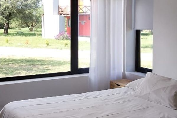 Dormitorio con ventanal y cortinas: Dormitorio luminoso con amplio ventanal, cortinas y ambiente cálido para el descanso.