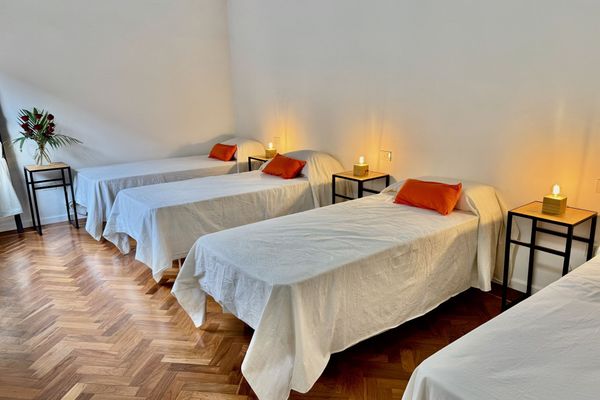 Dormitorio amplio con cuatro camas individuales, ideal para viajeros que buscan compartir. Ambiente luminoso y sereno, con detalles simples y funcionales. El piso de madera aporta calidez, mientras que la luz tenue crea una atmósfera tranquila.