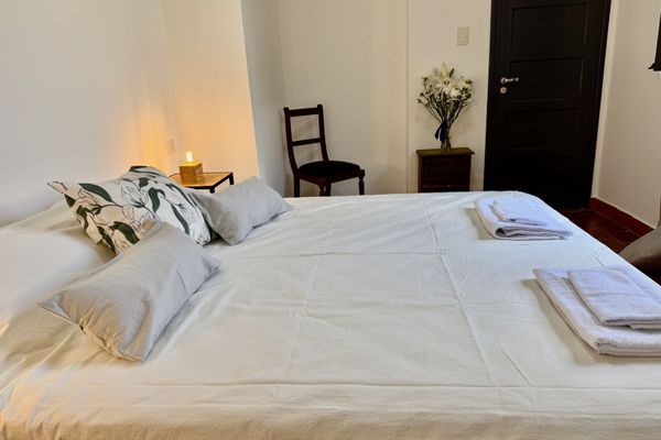 Dormitorio con cama blanca queen, aire acondicionado y luz natural. Ideal para descansar en un ambiente simple y cómodo.