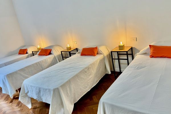 Dormitorio amplio con cuatro camas individuales, ideal para viajeros que buscan compartir. Ambiente luminoso y sereno, con detalles simples y funcionales. El piso de madera aporta calidez, mientras que la luz tenue crea una atmósfera tranquila.