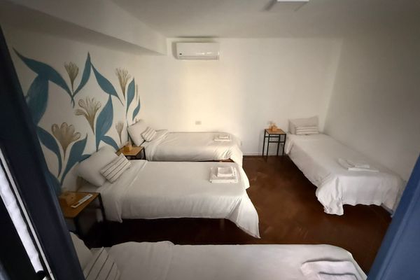Dormitorio luminoso con varias camas, veladores con lámparas cálidas y detalles naturales. Vista desde una pequeña abertura decorada con plantas que aporta un toque acogedor y relajado. Ideal para descansar en un ambiente sereno. Baño privado en Suite.