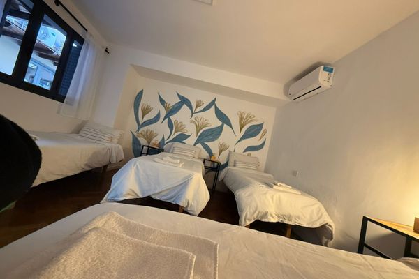 Dormitorio luminoso con varias camas, veladores con lámparas cálidas y detalles naturales. Vista desde una pequeña abertura decorada con plantas que aporta un toque acogedor y relajado. Ideal para descansar en un ambiente sereno. Baño privado en Suite.