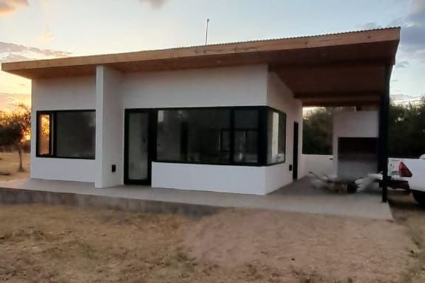 Vista exterior de la cabaña: Fachada de la Cabaña 1 con galería techada, asador y vistas panorámicas a las sierras.