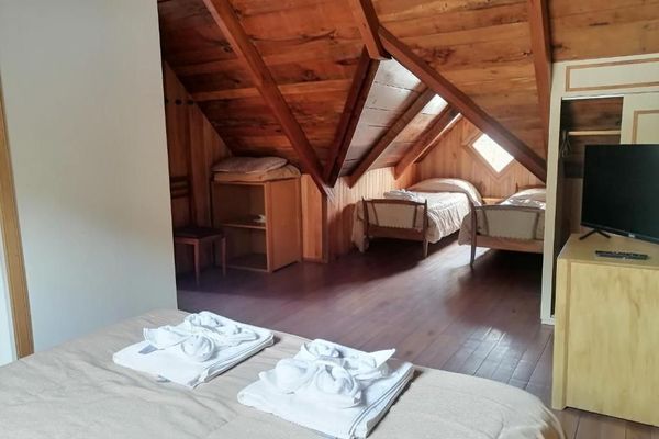 Interior de la habitación ‘Coihue’ en la hostería Wesley, con cama doble al frente y dos camas twin al fondo, bajo un techo de madera con ventana en forma de rombo
