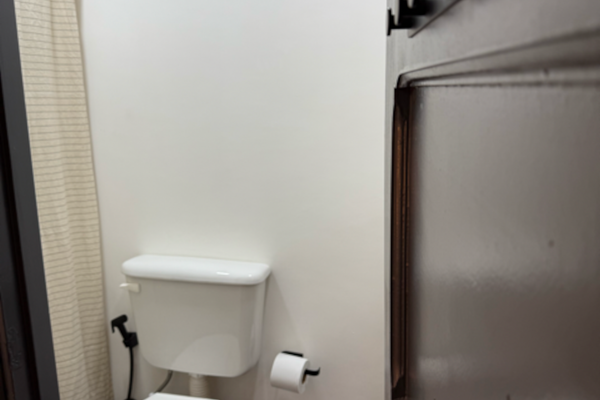 Baño compartido con ducha, equipado con sanitarios modernos y detalles minimalistas. Cuenta con lavamanos tipo bowl sobre estante negro, espejo redondo. Cortina de baño a rayas, tacho de residuos y toalla incluidos para mayor comodidad.