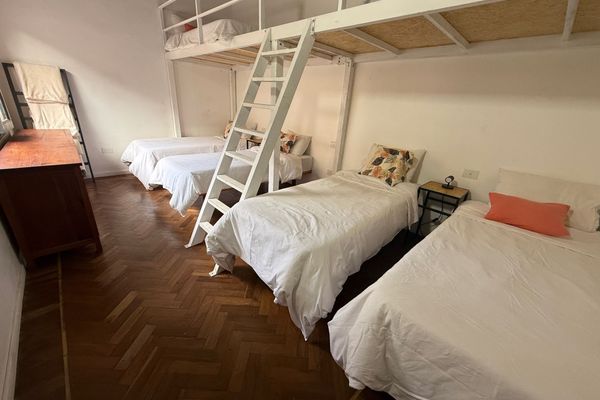 Amplia habitación con diseño de doble altura, tres camas individuales en planta baja y una cama en entrepiso. Los techos altos, el piso de madera y la luz natural crean un ambiente cómodo y acogedor.