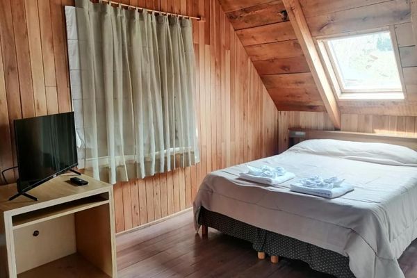 Ambiente acogedor de la habitación ‘Coihue’ en la hostería Wesley, con cama doble, cortinas claras y luz natural entrando por una ventana cenital.