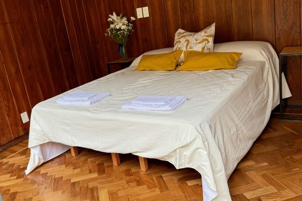 Habitación acogedora con cama matrimonial, revestida en madera y con piso de parquet. Cuenta con aire acondicionado, luz natural y vista al patio. Ideal para descansar en un entorno cálido, tranquilo y familiar.