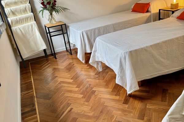 Dormitorio amplio con cuatro camas individuales, ideal para viajeros que buscan compartir. Ambiente luminoso y sereno, con detalles simples y funcionales. El piso de madera aporta calidez, mientras que la luz tenue crea una atmósfera tranquila.