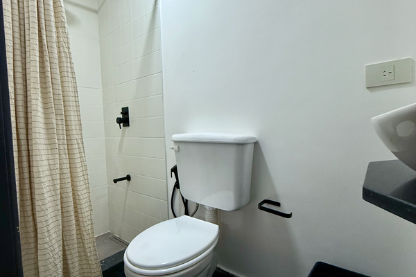 Baño compartido con ducha, equipado con sanitarios modernos y detalles minimalistas. Cuenta con lavamanos tipo bowl sobre estante negro, espejo redondo. Cortina de baño a rayas, tacho de residuos y toalla incluidos para mayor comodidad.
